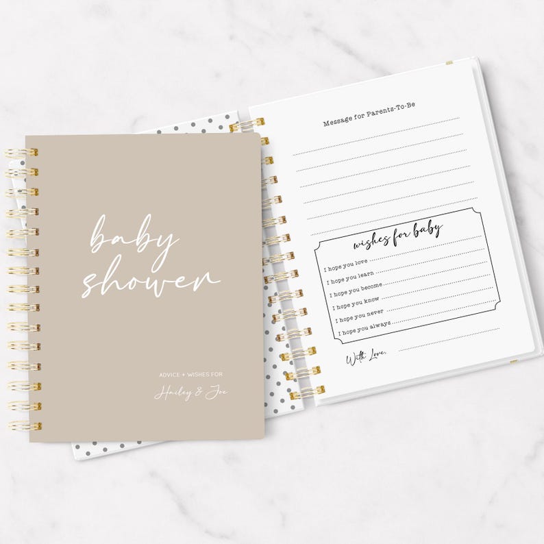 May include: A beige baby shower guest book with a gold spiral binding. The cover has the words "baby shower" written in white cursive script. The inside pages have lines for guests to write messages for the parents-to-be and wishes for the baby.