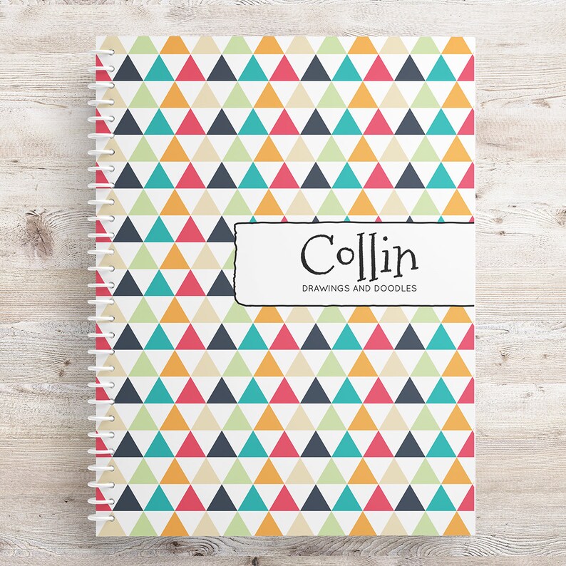 May include: A spiral bound notebook with a colorful geometric pattern of triangles in shades of teal, orange, pink, yellow, and gray. The cover has a white label with the name "Collin" and the text "Drawings and Doodles".