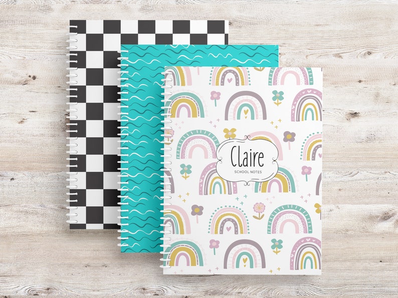 May include: Three spiral-bound notebooks with different cover designs. One has a black and white checkerboard pattern, another has teal wavy lines, and the third features a rainbow and floral design with the name "Claire" and "School Notes".