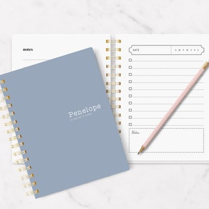 May include: A blue spiral bound notebook with the text "Penelope to do list + notes" on the cover. The notebook is open to a blank page with a calendar and a section for notes.