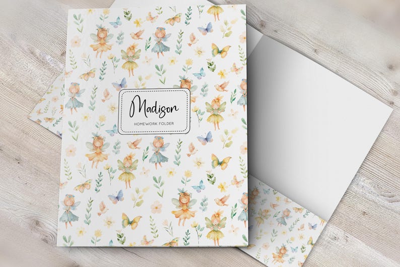 K&ouml;nnte beinhalten: Eine wei&szlig;e Hausaufgabenmappe mit einem sich wiederholenden Aquarellmuster aus kleinen Feen, Schmetterlingen und gr&uuml;nem Blattwerk. Ein zentrales rechteckiges Etikett zeigt den Namen Madison und den Text HOMEWORK FOLDER in schwarzer Schreib- und serifenloser Schrift.