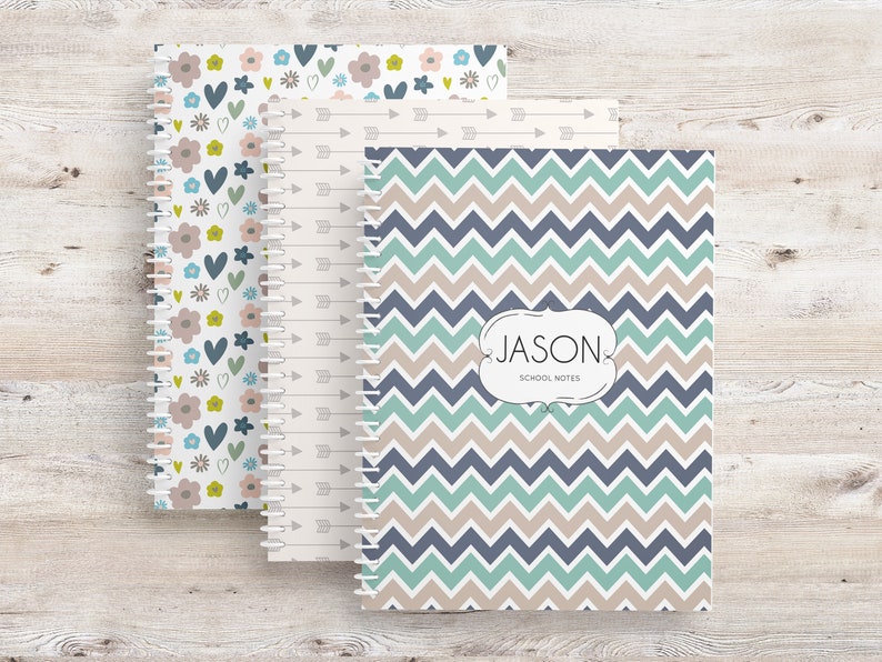 May include: Three spiral-bound notebooks with patterned covers. One features a floral design with blue, pink, and green accents. Another has a cream background with arrows. The third notebook has a blue, teal, and tan chevron pattern with the name "JASON" and "SCHOOL NOTES".