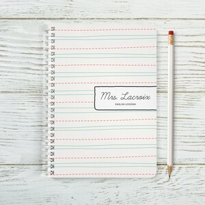 May include: A white notebook with red and green lines. The notebook has a spiral binding and a black label that says "Mrs. Lacroix English Lessons".