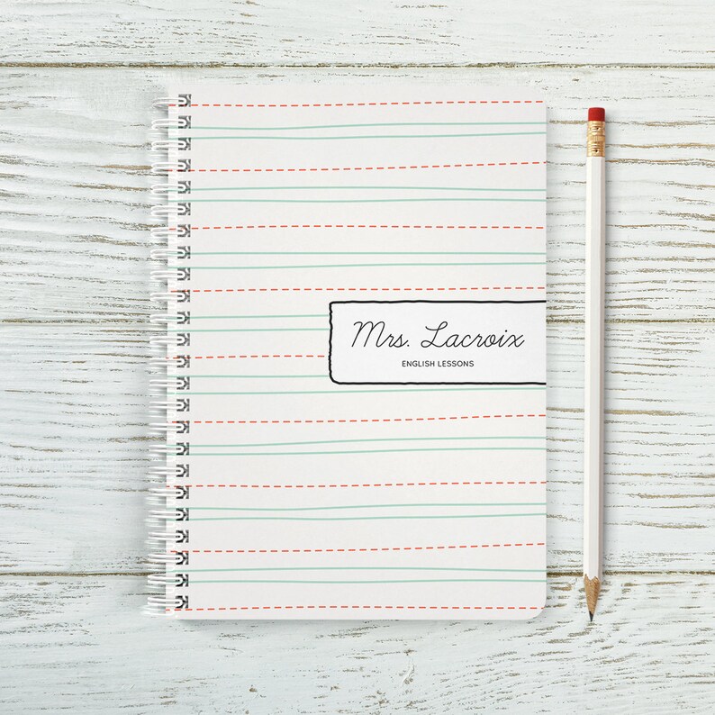 May include: A white notebook with red and green lines. The notebook has a spiral binding and a black label that says "Mrs. Lacroix English Lessons".