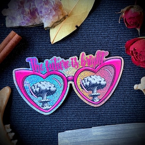 May include: Pink heart-shaped sunglasses with a glittery finish and the text "The future is bright" above the lenses. The lenses show a cartoon image of a mushroom cloud explosion.