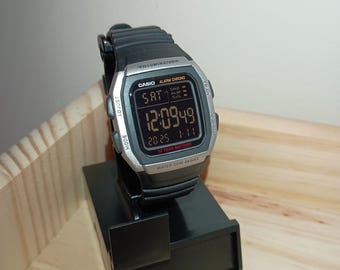 May include: A silver and black Casio digital watch with a black band. The watch face displays the time, date, and day of the week. The watch is water resistant and has a 10-year battery.