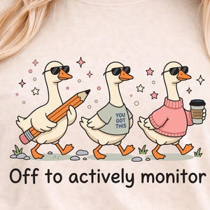 May include: Beige t-shirt featuring three cartoon geese wearing sunglasses. One goose holds a pencil, another a shirt that says "You Got This", and the third a coffee cup. The text "Off to actively monitor" is below the geese.