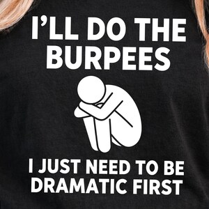 May include: Black t-shirt with the text "I'll Do The Burpees" in white, above a white graphic of a person sitting with their head on their knees. Below the graphic is the text "I Just Need To Be Dramatic First".