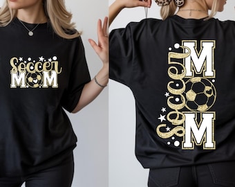 Peut inclure: T-shirt noir avec l'inscription "Soccer Mom" en lettres dorées pailletées, un graphisme de ballon de foot et des détails blancs. Le dos du t-shirt reprend le motif verticalement.