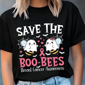 May include: Black t-shirt with the text "SAVE THE BOO-BEES Breast Cancer Awareness." The design features cartoon bees dressed as ghosts, spiderwebs, bats, and pink hearts. A pink ribbon is also included.