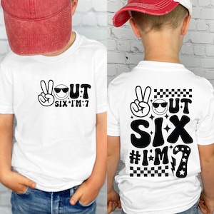 Peut inclure: T-shirt blanc avec un motif noir à l'avant et à l'arrière. Le motif avant comprend un signe de paix, un visage souriant portant des lunettes de soleil et le texte "OUT SIX I'M 7". Le motif arrière a les mêmes éléments avec un motif à carreaux.