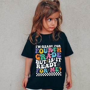 May include: A black t-shirt with the text "I'M READY FOR FOURTH GRADE BUT IS IT READY FOR ME?" in colorful, retro-style lettering. The shirt features a peace sign and a pencil graphic, with a checkered pattern at the bottom.