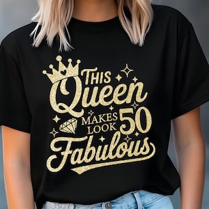 Op de afbeelding: Zwart T-shirt met gouden glittertekst: "This Queen Makes 50 Look Fabulous." Het ontwerp bevat een kroon, diamant en sterren. Het shirt heeft een ronde hals.