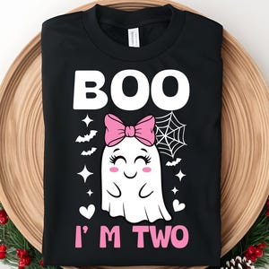 May include: Black t-shirt with a Halloween design. The shirt displays the word "BOO" in white, a ghost with a pink bow, and the text "I'M TWO" in pink. The design also includes bats, stars, a spiderweb, and hearts.