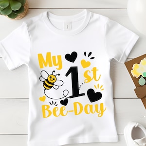May include: White toddler t-shirt with a "My 1st Bee-Day" design. The design features a cartoon bee, hearts, and text in yellow and black. A cute outfit for a first birthday celebration.
