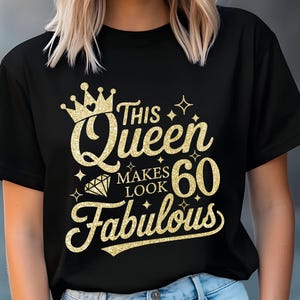 May include: Black t-shirt with gold glitter text that reads "This Queen Makes 60 Look Fabulous." The design includes a crown, diamond, and star accents. The shirt is a crew neck style.