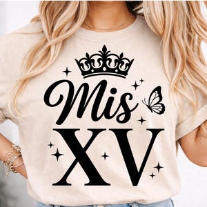 May include: Beige t-shirt with a black crown, the words "Mis XV", a butterfly, and the Roman numeral XV. The design includes star accents. The shirt has short sleeves.