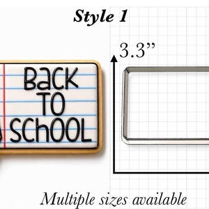 Op de afbeelding: Een koekje in de vorm van een potlood en een vel gelinieerd notitiepapier met de tekst Back To School, naast een metalen uitsteekvormpje. De vorm meet 8,38 cm hoog en 12,7 cm breed op een achtergrond met een raster.