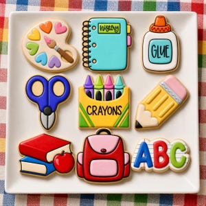 Op de afbeelding: Een set van negen school-thema koekjes in de vorm van een verfpalet, geschrift-notitieboek, lijmfles, blauwe schaar, doosje kleurpotloden, geel potlood, twee gestapelde boeken met een appel, een rode rugzak en de letters ABC.