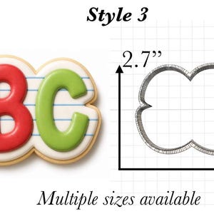 Op de afbeelding: Een koekjesvorm in de vorm van de letters ABC met een lijntjespapier-ontwerp, 6,86 cm hoog en 12,7 cm breed. De vorm staat naast een koekje versierd met blauw, rood en groen glazuur op een witte achtergrond.