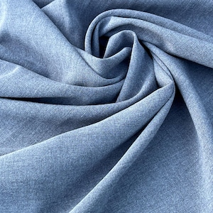 May include: Close-up of a light blue fabric with a textured appearance. The fabric is draped and folded, creating soft shadows and highlights. The material appears to be a medium-weight textile, suitable for various sewing projects.