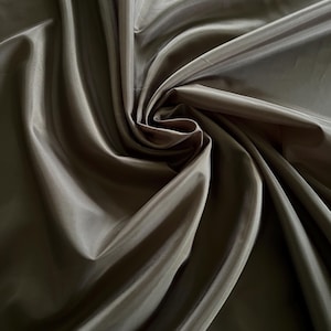 May include: A close-up shot of olive-green fabric, swirled and folded. The material has a silky sheen, with shadows and highlights. The fabric appears smooth and flowing, with a slight sheen. The texture suggests a luxurious textile, possibly for clothing or home decor.