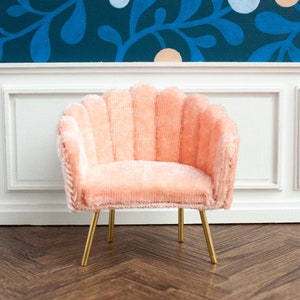 May include: A pink velvet armchair with a scalloped back and gold metal legs. The chair is sitting on a wood floor.