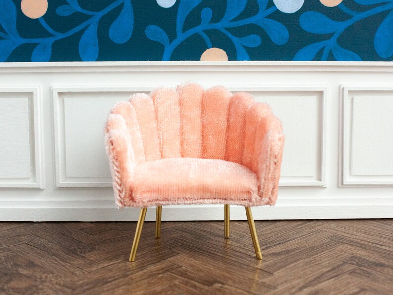 May include: A pink velvet armchair with a scalloped back and gold metal legs. The chair is sitting on a wood floor.