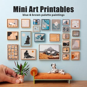 Op de afbeelding: Een verzameling miniatuur ingelijste kunstprints in een blauw en bruin kleurenschema, tentoongesteld op een muur met een kleine plant in een pot en een miniatuurbank met een dalmatienbeeldje erop. De tekst "Mini Art Printables" en "blue & brown palette paintings" wordt boven de kunstprints weergegeven.