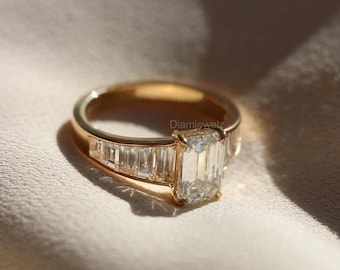 May include: A gold engagement ring featuring a large emerald-cut diamond and a band of smaller baguette diamonds.