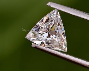 Può includere: Una gemma di diamante trasparente di forma triangolare, tenuta da una pinza su uno sfondo verde.