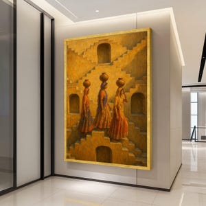 May include: An oil painting depicts three women in traditional attire walking up stone steps, each balancing a water pot on their head. The artwork features warm tones of orange, yellow, and brown, with a gold frame. The scene evokes a sense of cultural heritage.