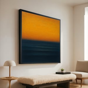 Op de afbeelding: Groot abstract schilderij met zwarte lijst. Het kunstwerk toont een kleurengradiënt, met een helder geel bovenaan dat overgaat in een diepblauw aan de onderkant, wat doet denken aan een zonsondergang boven de oceaan.