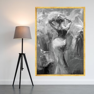 Puede incluir: Pintura abstracta en blanco y negro de una figura con los brazos levantados, enmarcada en oro. Una lámpara de pie trípode negra con una pantalla gris se encuentra a la izquierda de la obra, contra una pared blanca.
