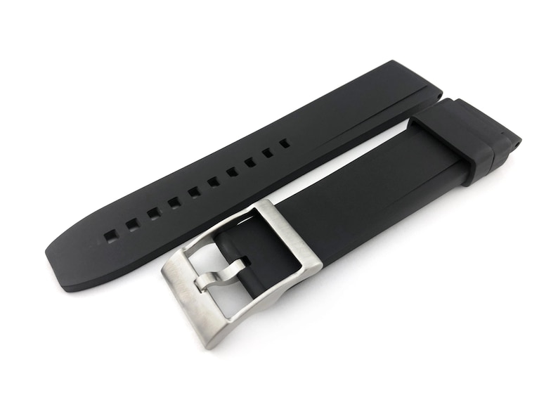 May include: A black silicone watch strap with a silver buckle. The strap has a textured surface and is designed for a watch with a 22mm lug width.