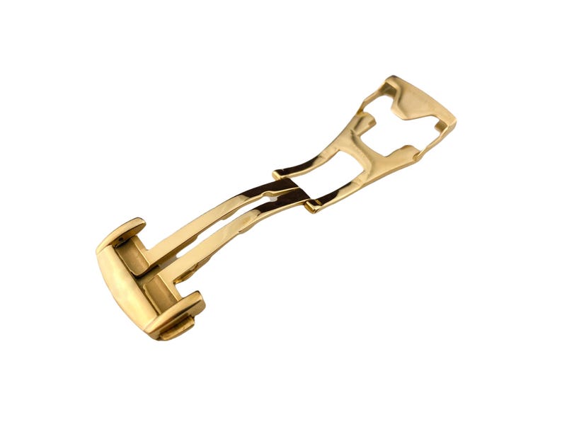 May include: A gold-colored watch clasp, designed with a curved, elongated shape. The clasp features a dual-hinge mechanism and a polished finish, reflecting light. The design suggests a luxury watch component.