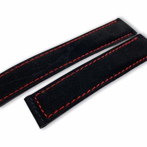 May include: Two black watch straps with red stitching. The straps are rectangular and made of a soft, textured material. The red stitching provides a contrasting detail.