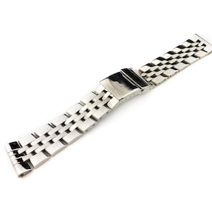 May include: A silver metal watch band with a clasp. The band has a brushed finish and is made of interlocking links.