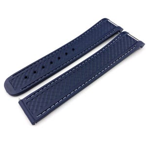 May include: Two-piece navy blue watch strap with white stitching. The strap has a textured surface and is designed to attach to a watch face. The strap is made of a flexible material and is shown against a white background.
