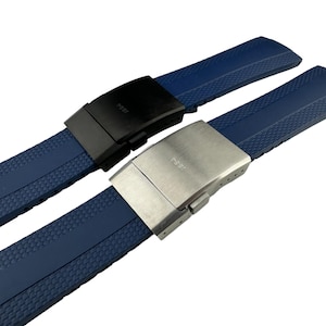 Könnte beinhalten: Zwei blaue Silikon-Uhrenarmbänder mit unterschiedlichen Metallschließen. Das obere Armband hat eine schwarze Schließe mit dem Aufdruck "FOSSIL". Das untere Armband hat eine silberne Schließe mit dem Aufdruck "FOSSIL".