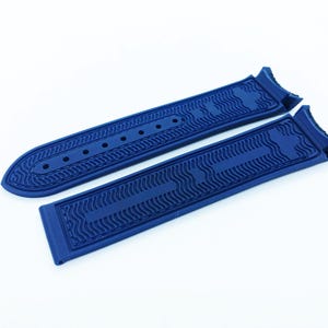 May include: Two pieces of a deep blue watch strap, featuring a textured wave pattern and multiple holes for adjustment. The strap is made of a flexible material and is designed to attach to a watch face. The design is modern and sleek.
