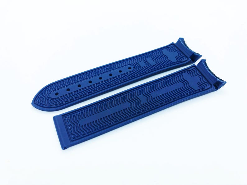 May include: Two pieces of a deep blue watch strap, featuring a textured wave pattern and multiple holes for adjustment. The strap is made of a flexible material and is designed to attach to a watch face. The design is modern and sleek.