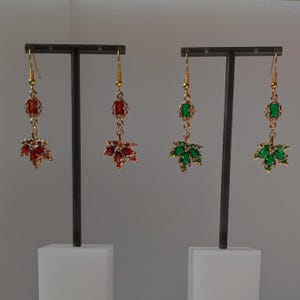 Peut inclure: Deux paires de boucles d'oreilles pendantes suspendues à des supports en T noirs. Une paire présente des cristaux rouges rectangulaires et en forme de feuille sur des montures dorées. L'autre paire présente des cristaux verts similaires.