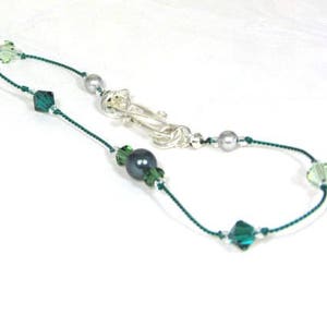 May include: A delicate green and silver necklace with a dark grey pearl and crystal accents.