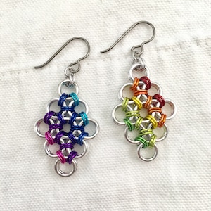 May include: A pair of rainbow colored earrings with a silver hook. The earrings are made of small metal rings that are linked together in a flower shape. The rings are colored in a rainbow pattern, with red, orange, yellow, green, blue, indigo, and violet.