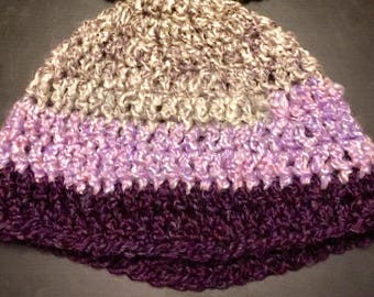 May include: A crocheted hat with three stripes of different colors. The top stripe is a light beige, the middle stripe is a light purple, and the bottom stripe is a dark purple.