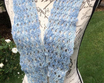 Peut inclure: Une écharpe en crochet dans un dégradé de couleurs bleu clair et blanc. L'écharpe est de forme triangulaire et présente un motif délicat et ajouré.