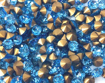 Può includere: Un assortimento di strass blu e oro scintillanti. Gli strass blu sono sfaccettati, riflettendo la luce, mentre quelli dorati hanno una forma metallica a piramide. Questi abbellimenti decorativi sono ideali per l'artigianato e la creazione di gioielli.
