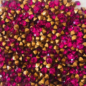 Könnte beinhalten: Nahaufnahme einer Sammlung funkelnder Strasssteine. Das Bild zeigt eine Mischung aus goldenen und magentafarbenen Strasssteinen, die eine lebendige Darstellung erzeugt. Die Strasssteine sind eng aneinander angeordnet und füllen den Rahmen.