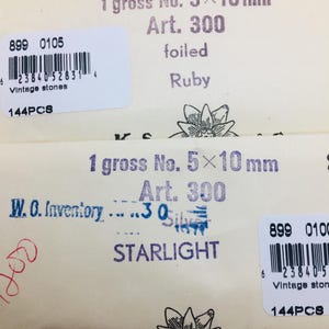 May include: Close-up of vintage stone packaging. The packaging includes text such as "1 gross No. 5x10mm", "Art. 300", and "Ruby". The packaging also includes a barcode and the text "Vintage stones".